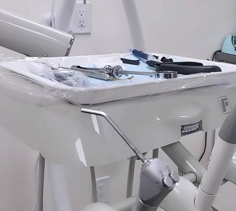The image shows a dental office setup with a dental chair, instruments, and tools on a tray, indicating a dental examination or treatment room.