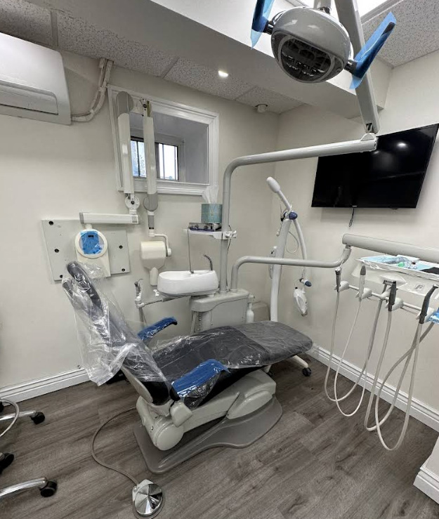 The image shows a dental office interior with various equipment and fixtures such as dental chairs, a large screen, a computer monitor, a dental light, a window, and a door.