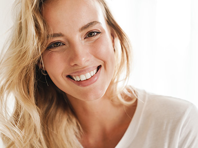 The image features a woman with blonde hair smiling at the camera. She has fair skin and is wearing a white top.