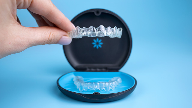 A person s hand holding an open dental impression tray with clear plastic teeth molds.