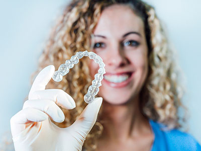 A woman holding a transparent dental implant with a smile.