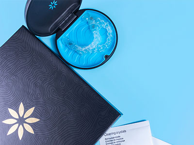 An open blue toothbrush case with a toothbrush inside on a light blue background, next to a black box with a floral design and text.