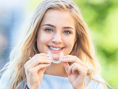 A woman with a toothy smile holding up a clear plastic aligner tray.