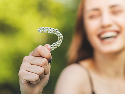 An adult female with a radiant smile holds up a transparent plastic dental retainer.