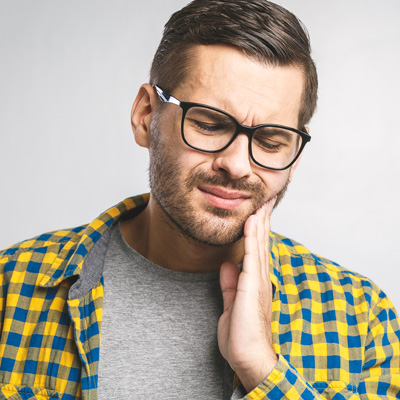 A man with glasses and a beard is clenching his teeth, possibly in pain or discomfort.