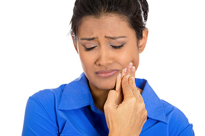 The image shows a woman with her eyes closed, holding her nose, seemingly in pain or discomfort. She appears to be indoors and is wearing a blue shirt.