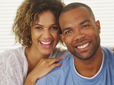 Man and woman smiling at camera, embracing each other with joyful expressions.