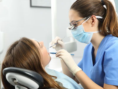 A woman sitting in a dental chair receiving dental treatment from a dentist wearing protective gear.