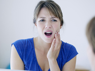 The image shows a woman with her mouth open, looking concerned or surprised, with her hand on her chin, and she appears to be indoors, possibly in a bathroom or bedroom setting.