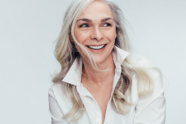 This is a photograph of a woman with blonde hair and a neutral expression, wearing a dark top and looking directly at the camera.