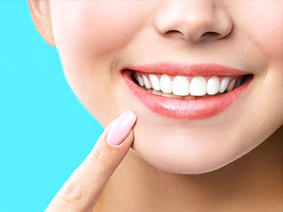 The image shows a close-up view of a person s face with a bright smile, highlighting their teeth and lips, against a blue background.